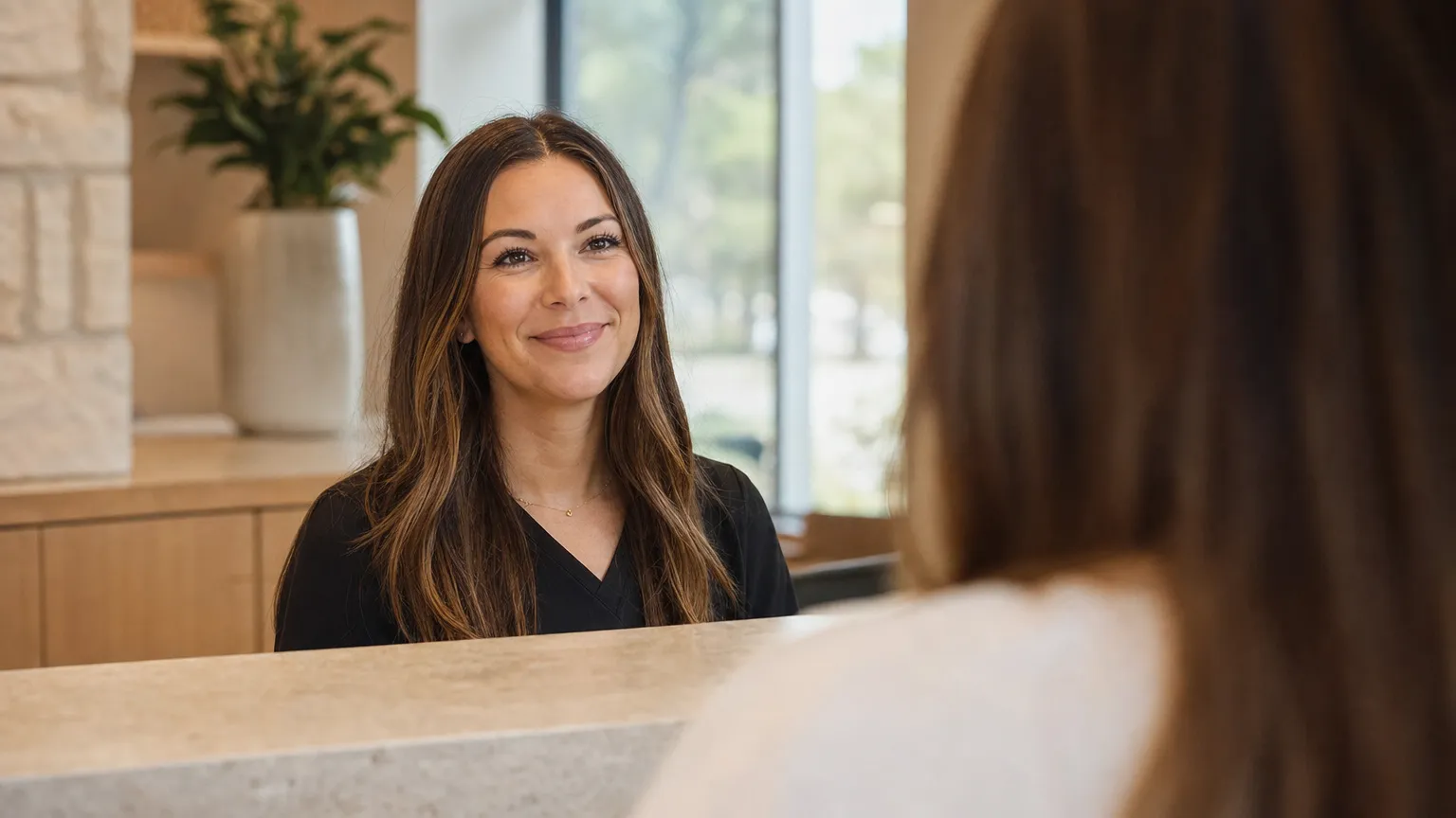 A receptionist smiling at an arriving patient across the front desk