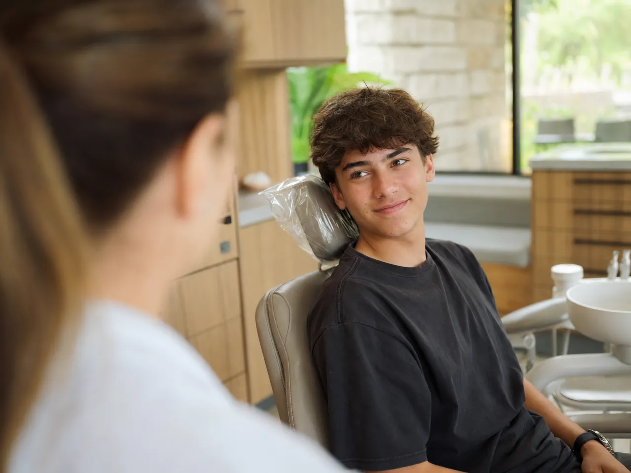 A relaxed teenager sitting in a dental chair, talking with a clinician