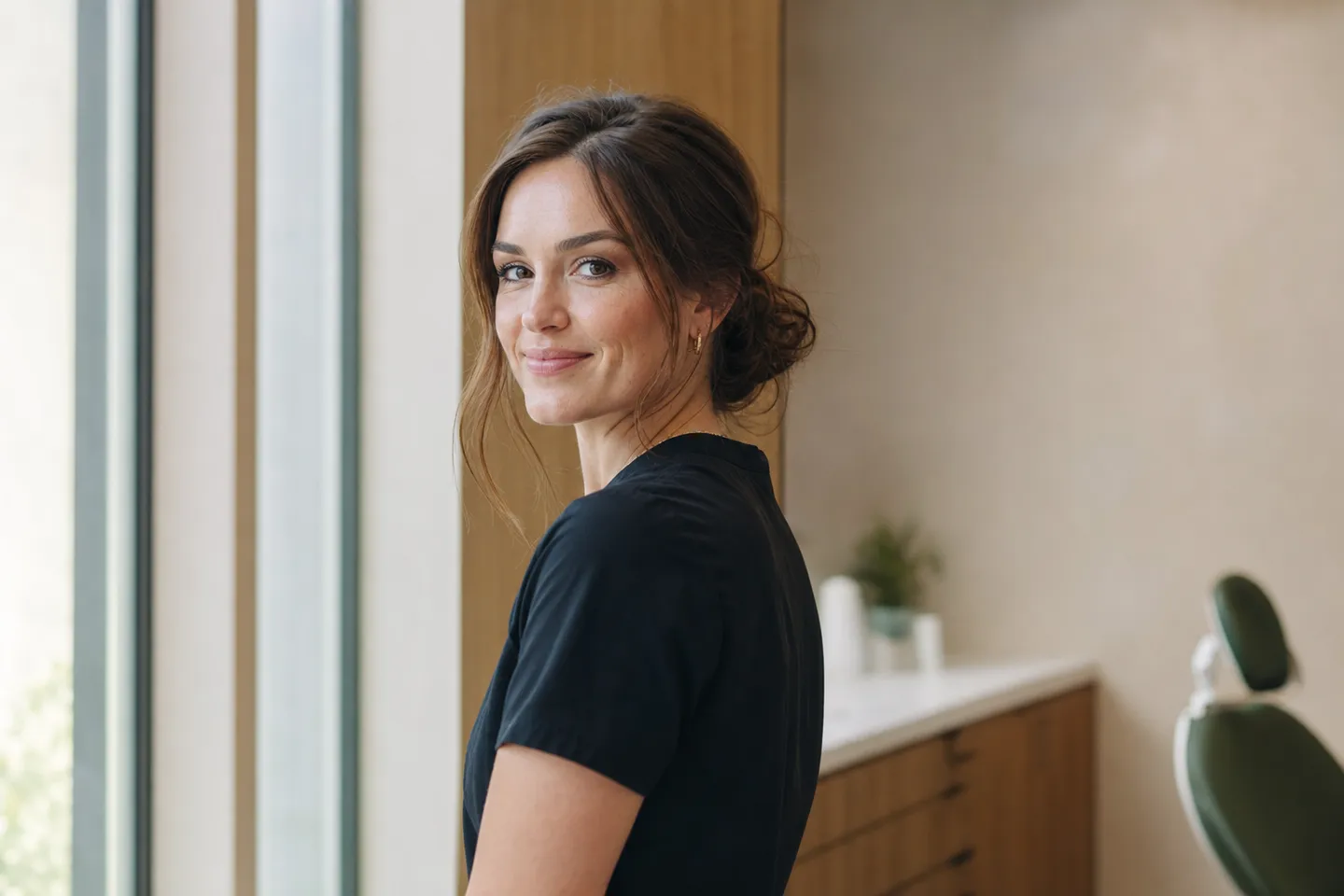 A woman standing by a window with a natural, confident smile